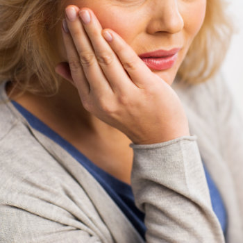 senior aged woman holds her cheek in pain