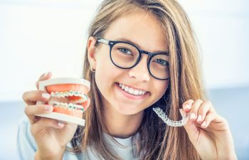 Young womanwith a perfect smile holding an invisible aligner in one hand and a dental model with traditional braces in the other one