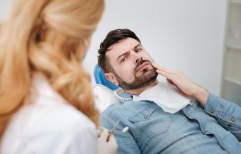 a concerned man in a dental chair discussing the treatment with a dentist