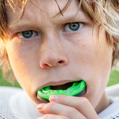 A boy with blonde hair putting in a green mouthguard between his teeth before the match.