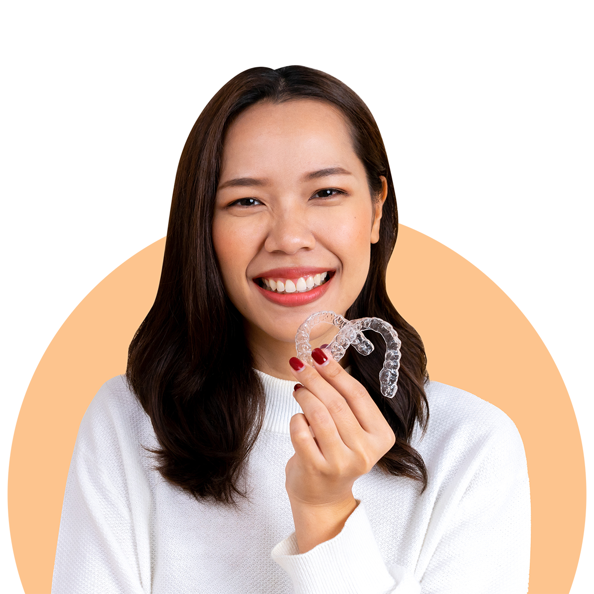 A smiling woman holds up a clear dental aligner against an orange background, wearing a white sweater.